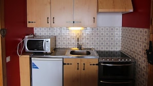 A compact kitchen with wooden cabinets, a microwave, a sink, and an oven. - Cozy Studio for 4 with South-Facing Balcony, Near Slopes and Shops - Pet Friendly (Huez)