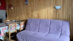 A cozy room with a purple sofa, wooden walls, a dining table with chairs, and a hanging light fixture. - Cozy Studio for 4 with South-Facing Balcony, Near Slopes and Shops - Pet Friendly (Huez)