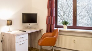 Een kamer met een bureau, een stoel, een televisie, een raam met gordijnen en een radiator.