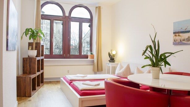 Een moderne hotelkamer met een groot raam, een rode bank, een ronde eettafel en een potplant.
