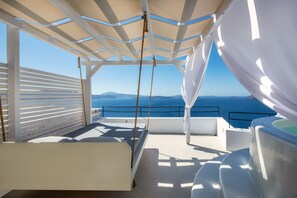 Um deck ao ar livre banhado pelo sol, com uma cama, uma banheira de hidromassagem e vista para o mar.