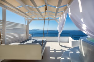 Terraza al aire libre iluminada por el sol con una cama, un jacuzzi y vistas al mar.
