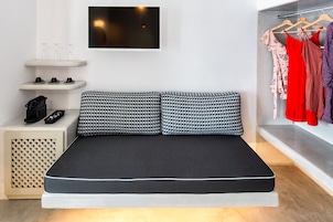 Un dormitorio moderno con una cama, un televisor, un armario y un estante con vasos y tazas.