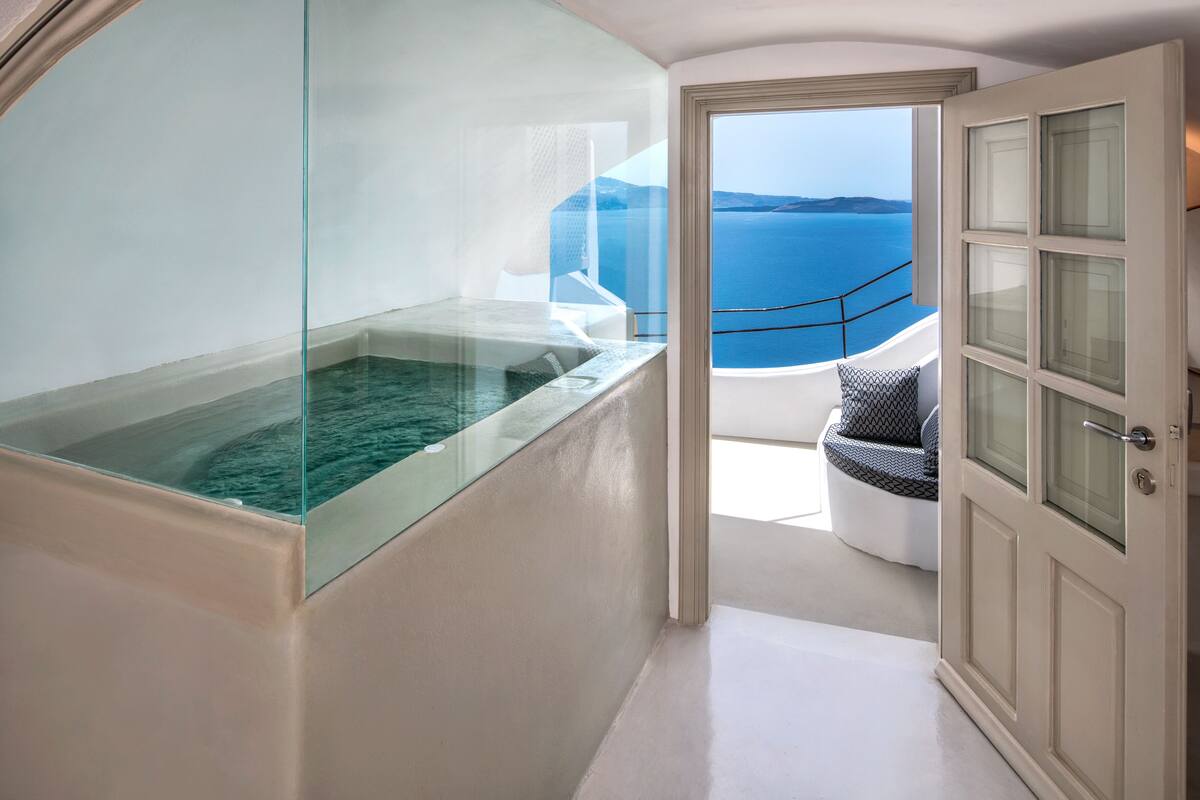 Une salle de bain moderne avec un jacuzzi entouré de parois de verre, un balcon offrant une vue sur la mer et une porte donnant sur un espace détente.