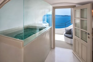Un baño moderno con jacuzzi de vidrio, un balcón con vistas al mar y una puerta que da a un área de estar.