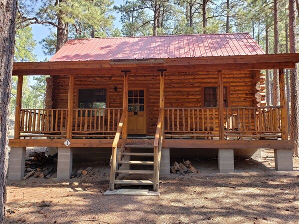 A log cabin with a red metal roof, a front porch with a wooden railing, and a staircase leading to the entrance.