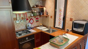 Eine Küche mit Gaskochfeld, Backofen, Spüle und Mikrowelle. Auf der Arbeitsfläche steht eine Obstschale und ein Korb mit Gläsern.