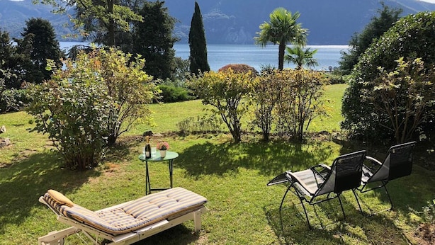 Ein Garten mit Liegestuhl, Stühlen und einem kleinen Tisch mit einer Flasche und Blumen.