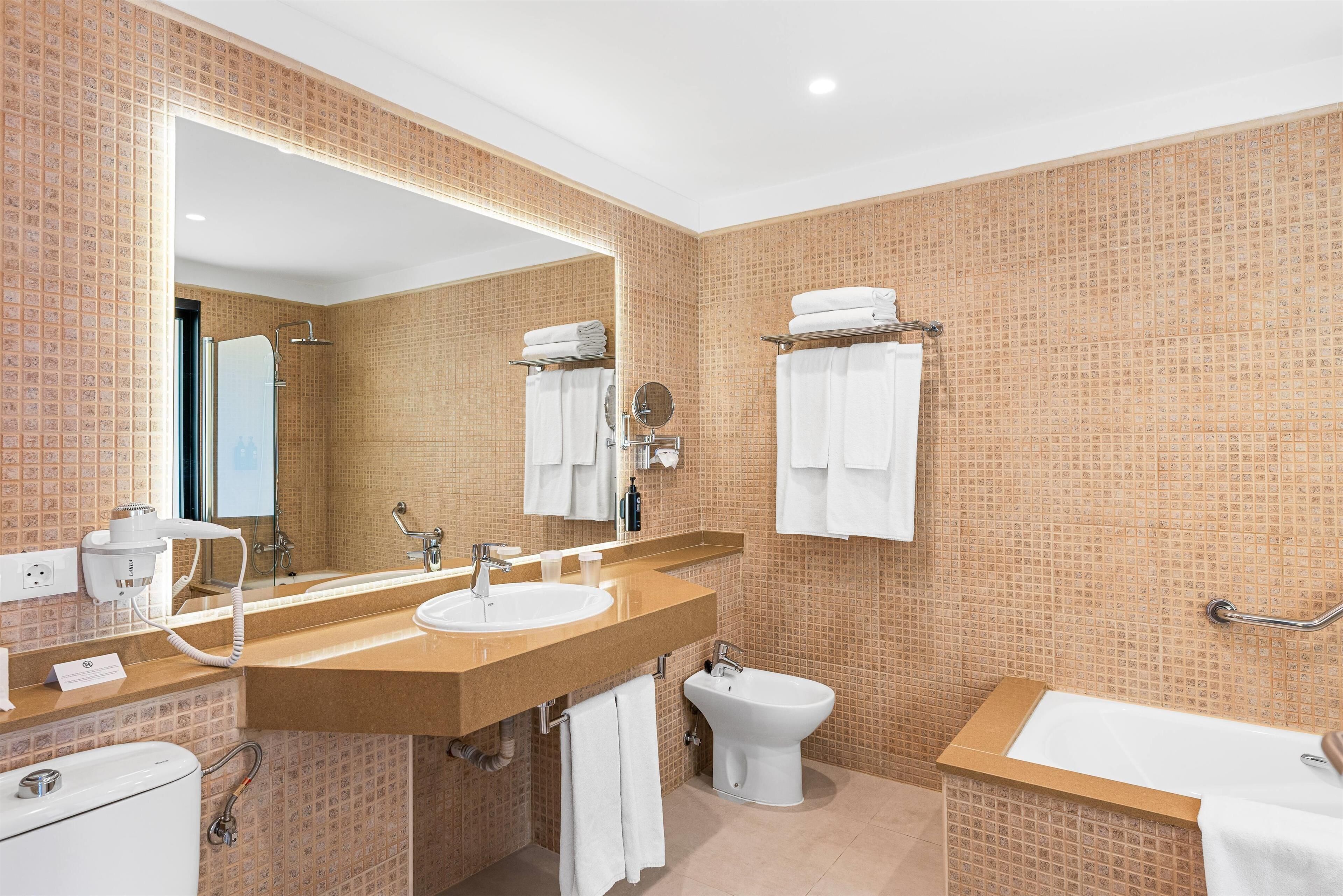 A modern bathroom with a large mirror, two sinks, a bidet, and a bathtub.