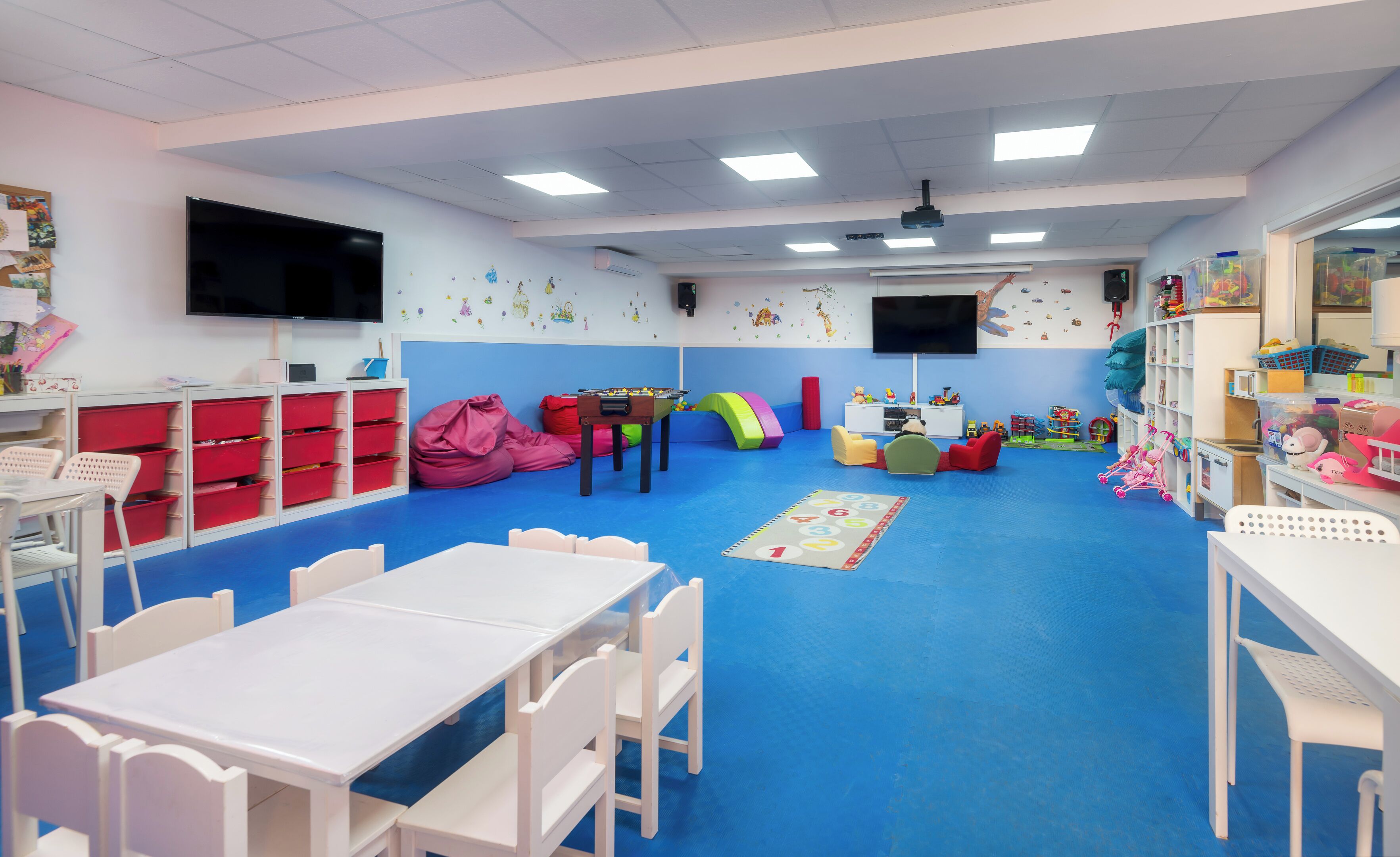 A children's playroom with a blue carpet, white furniture, and colorful decorations.