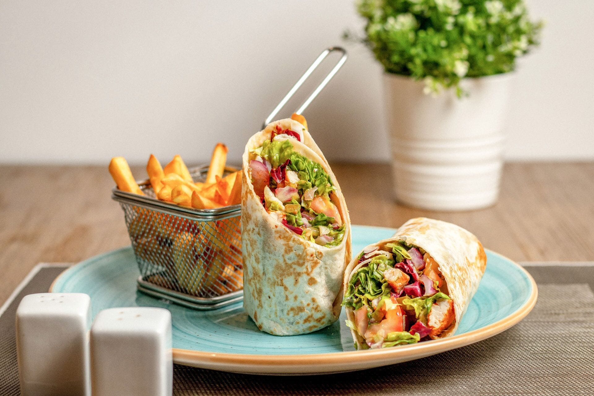 A plate with a wrap and a basket of fries.