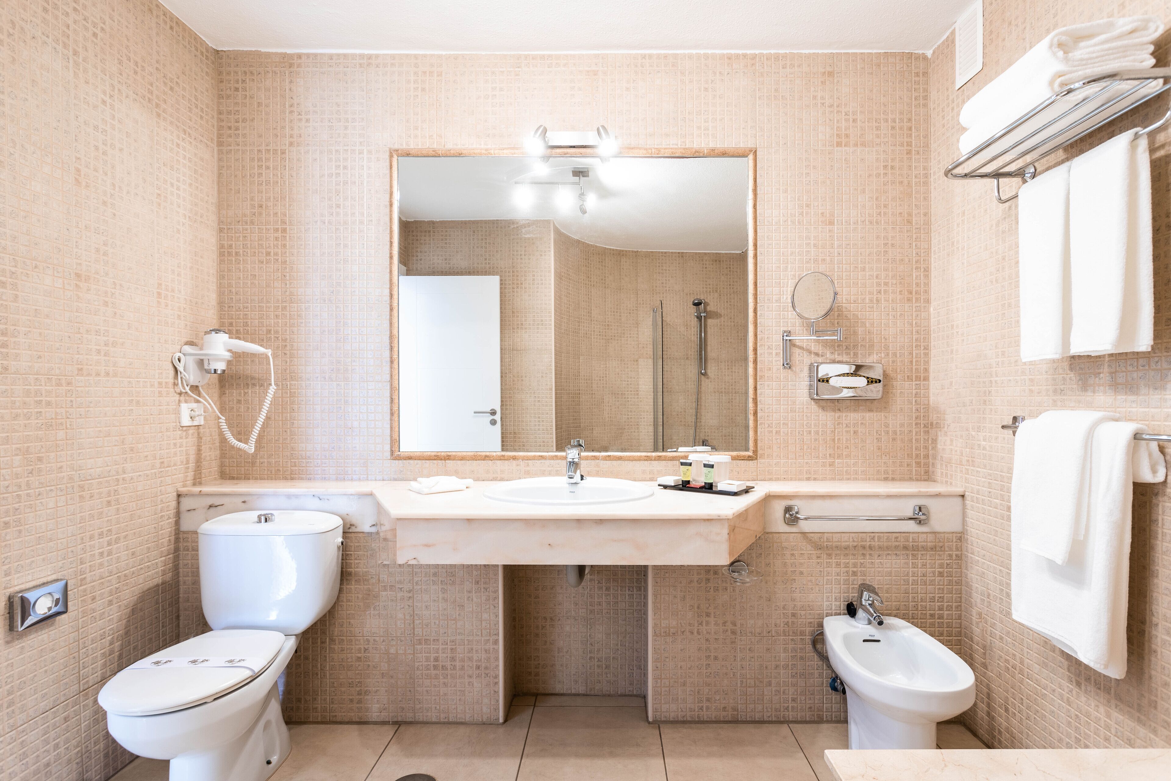 A modern bathroom with a toilet, bidet, sink, and mirror.