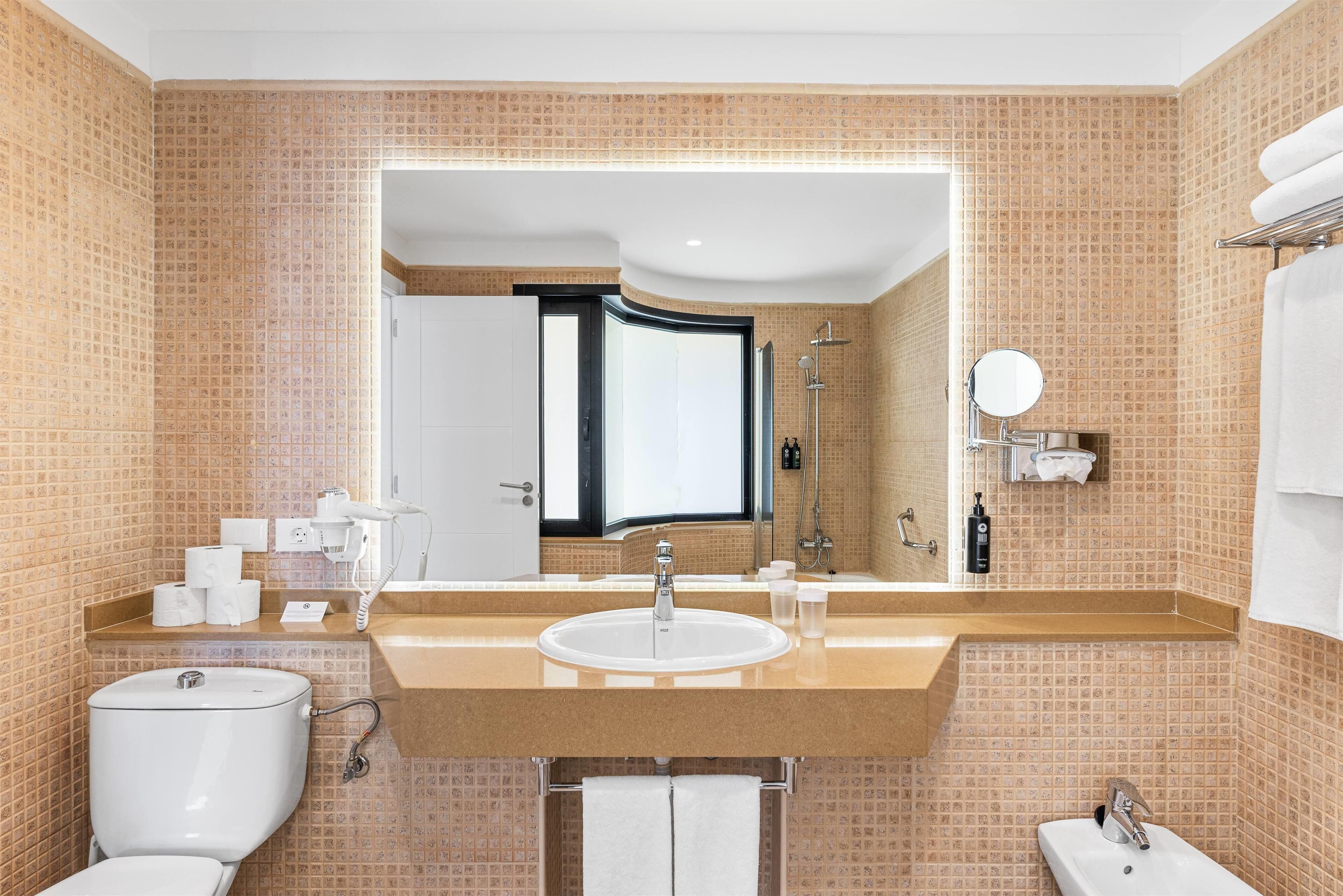 A modern bathroom with a large mirror, a sink, a toilet, and a shower area.