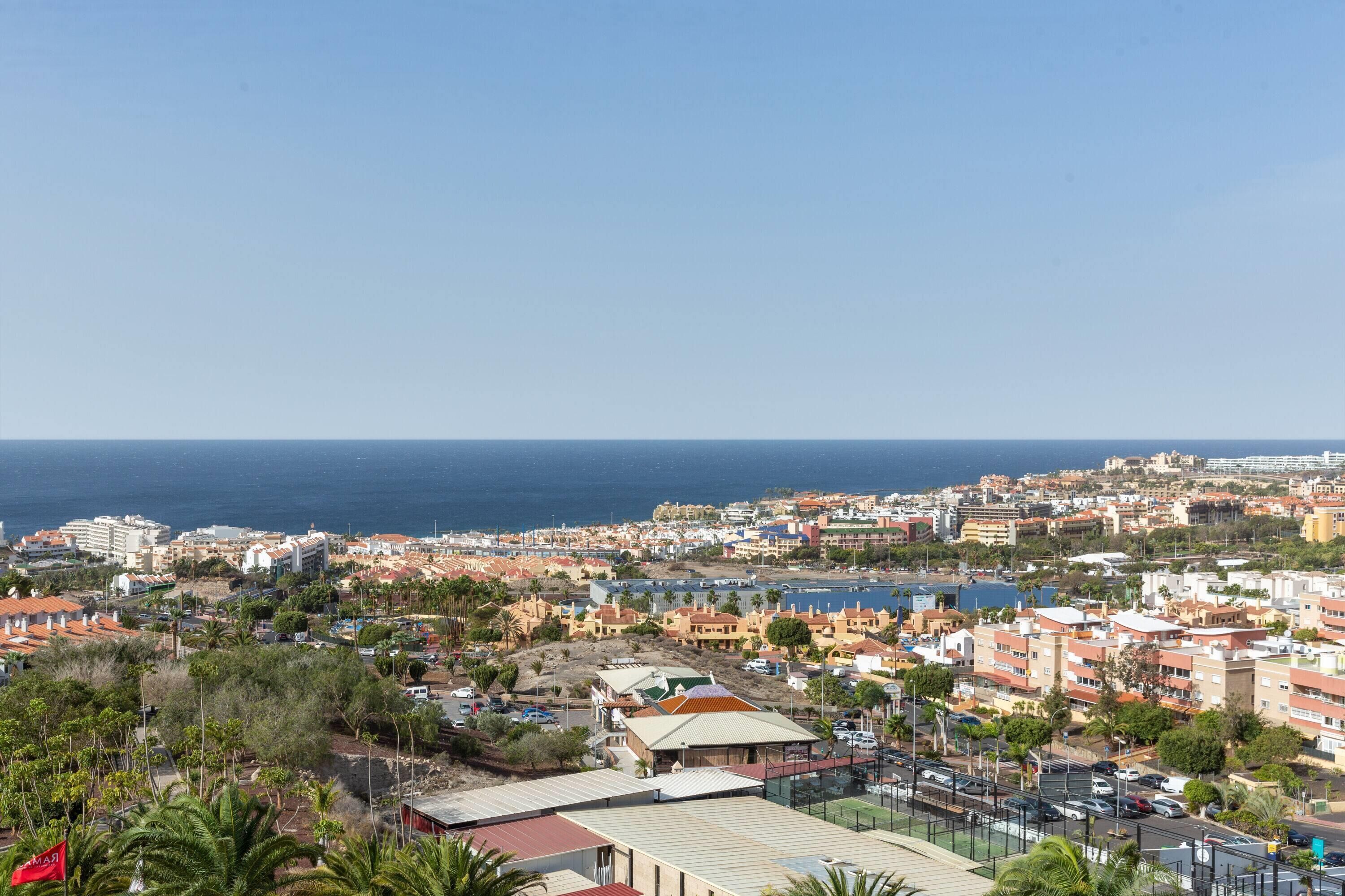 A coastal cityscape with a mix of residential and commercial buildings, a clear blue sky, and the ocean in the background.