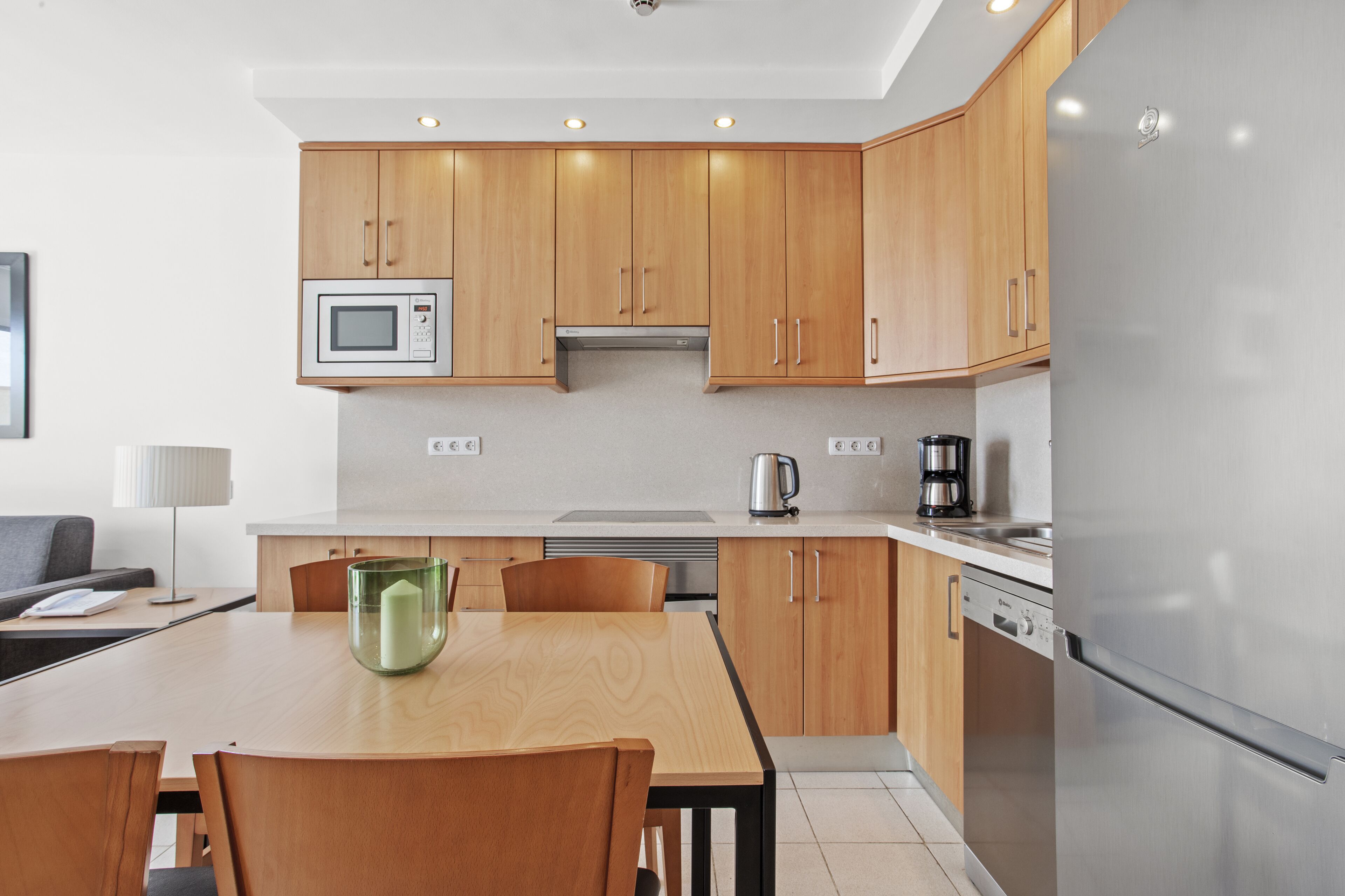 A modern kitchen with wooden cabinets, a stainless steel refrigerator, a microwave, and a coffee maker.