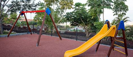 Un parque infantil con un tobogán amarillo y columpios.