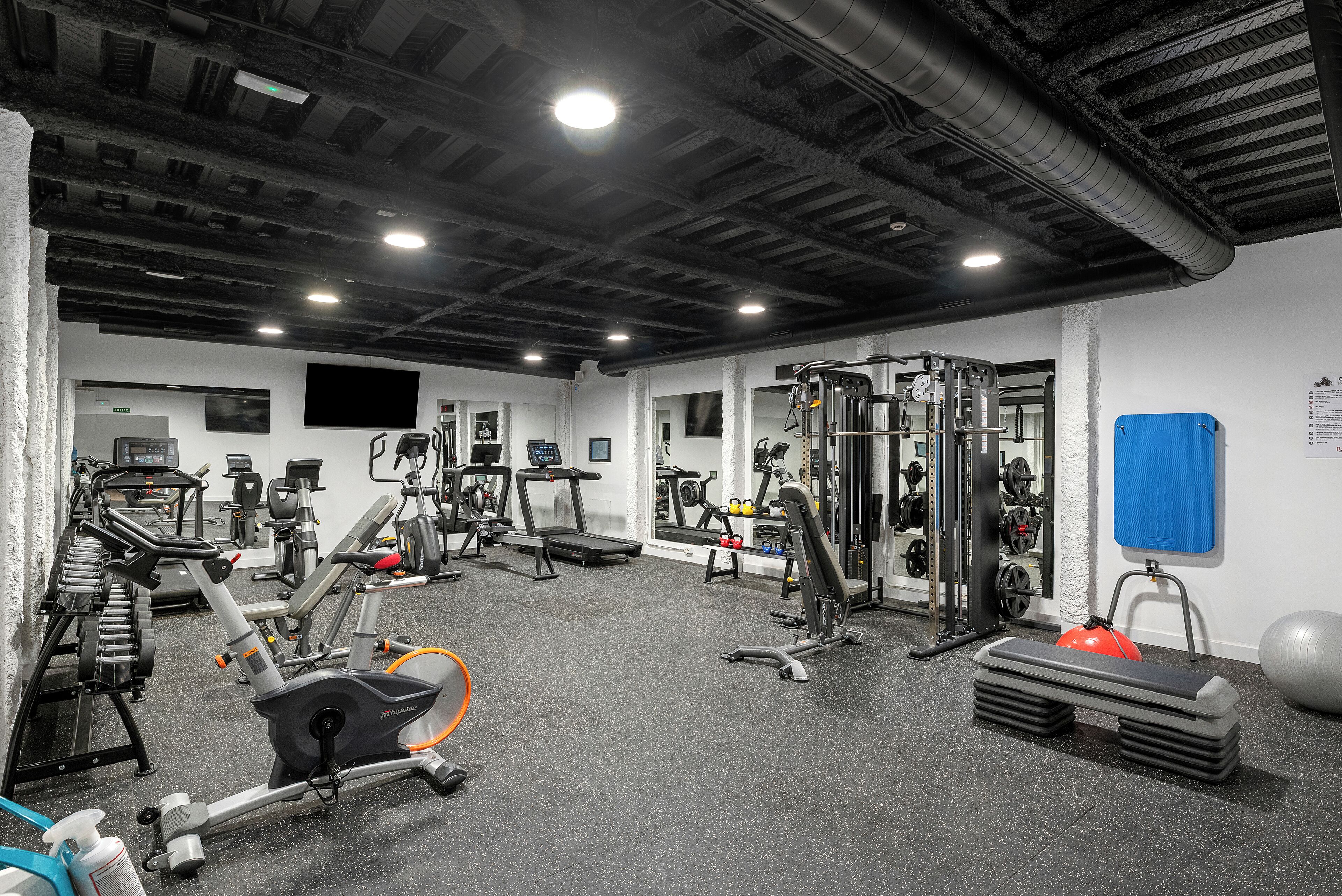 Une salle de sport équipée de divers appareils d’entraînement, notamment des tapis de course, des appareils de musculation et un rameur.