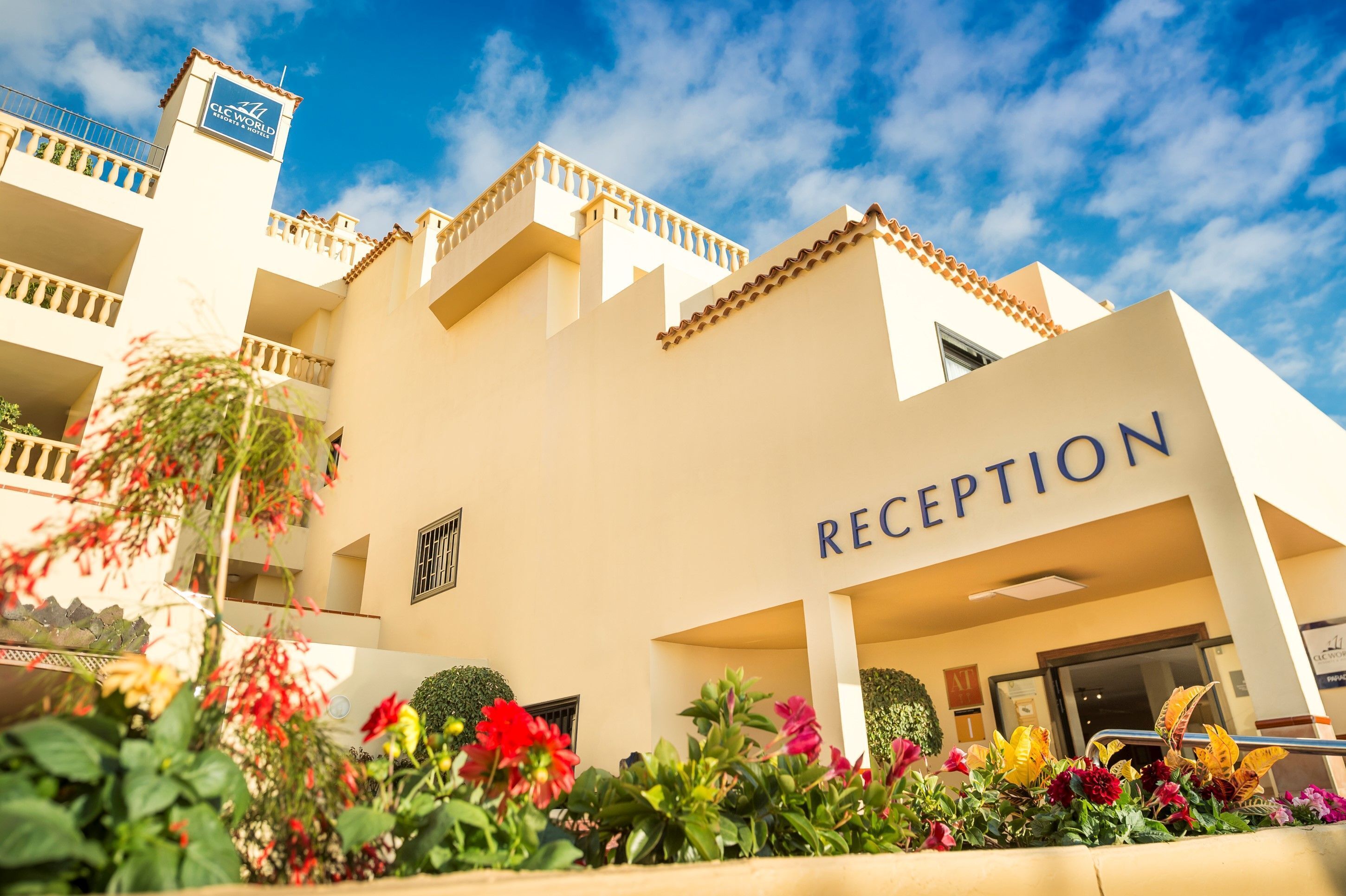 Ein Hotel mit Rezeption, einem Balkon und einem gepflegten Garten mit verschiedenen Pflanzen und Blumen.