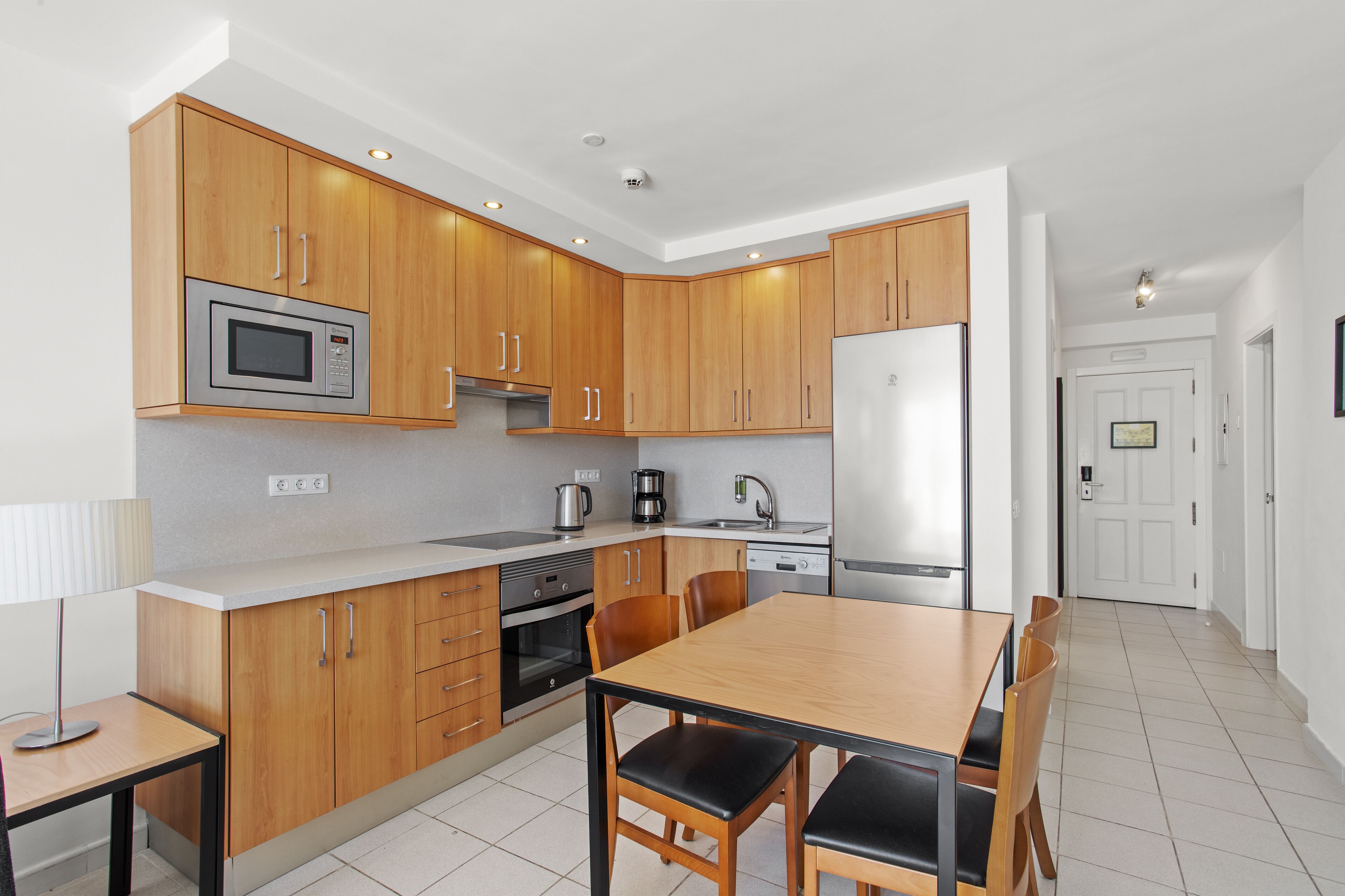 Una cocina moderna con armarios de madera, electrodomésticos de acero inoxidable y una zona de comedor con mesa y sillas.