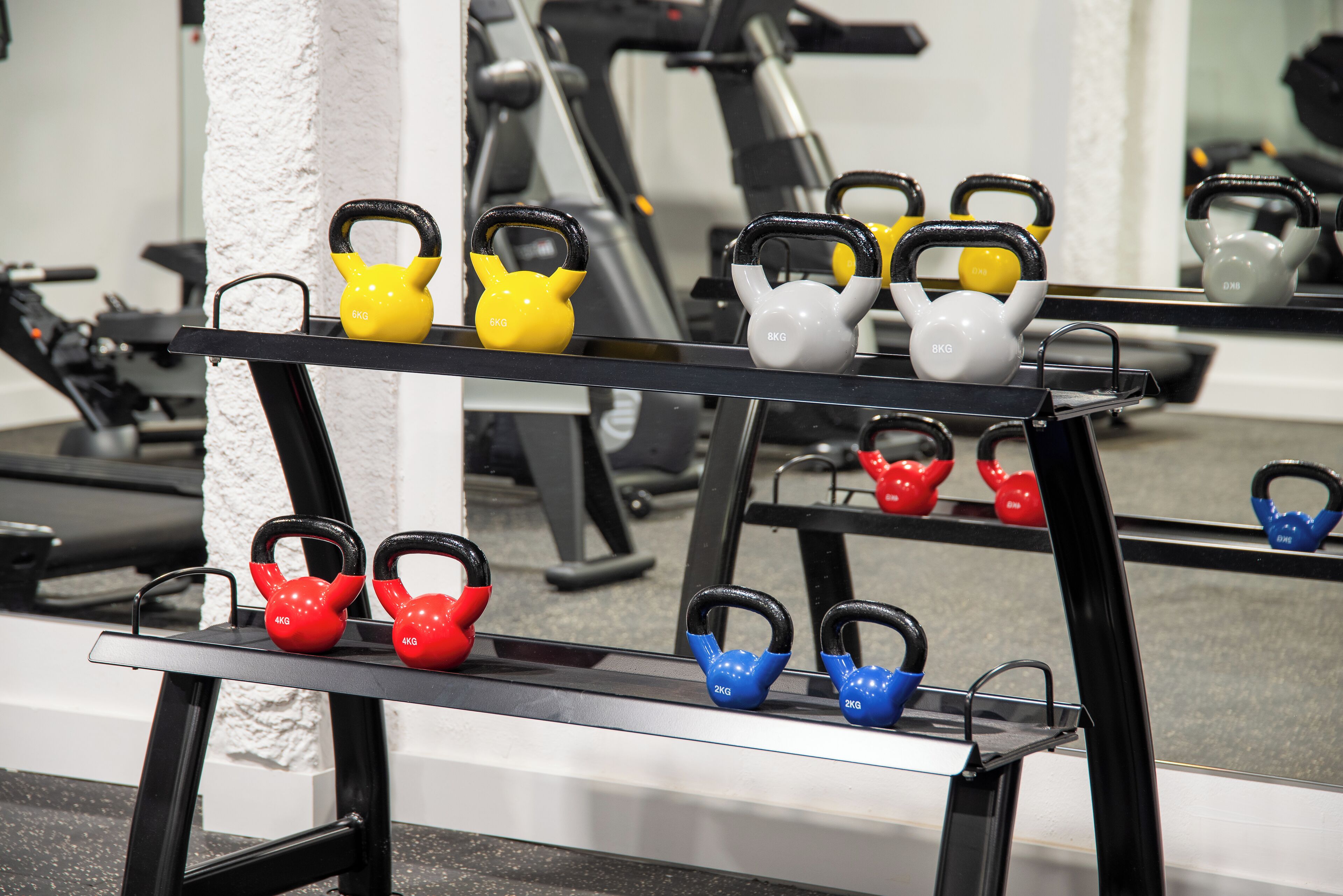 Une salle de sport où l’on trouve des kettlebells de différents poids et de différentes couleurs, disposées sur des étagères.