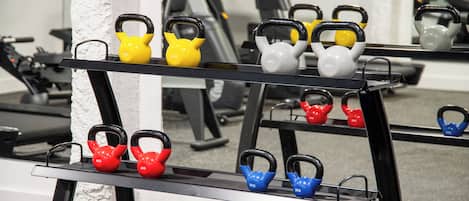 Kuntosali, jossa on eripainoisia ja -värisiä kettlebell-painoja järjestettynä telineille.