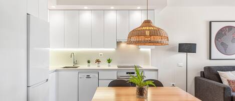 Una cocina moderna con armarios blancos, una mesa de comedor de madera y una lámpara colgante de ratán.