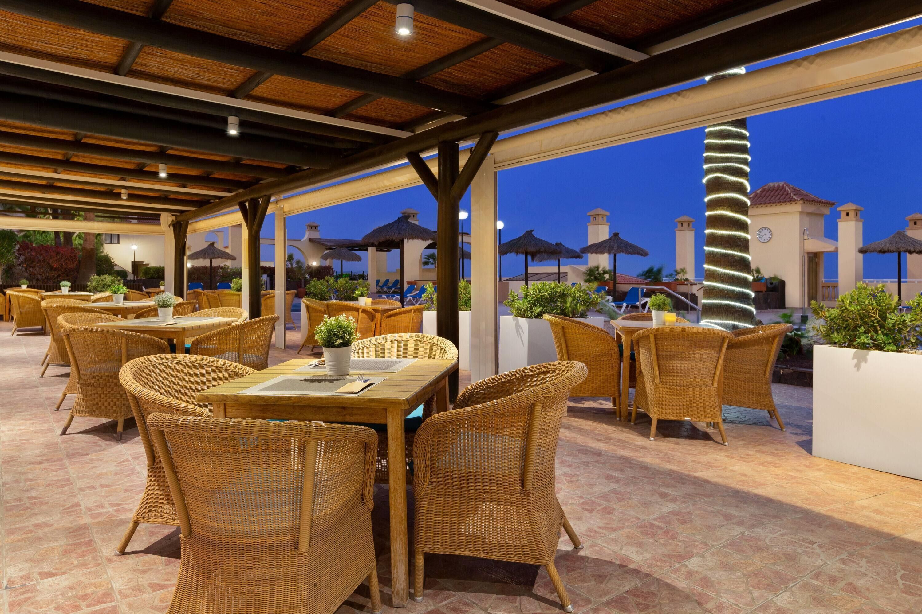 An outdoor patio area with wicker furniture and umbrellas, featuring a view of buildings in the background.