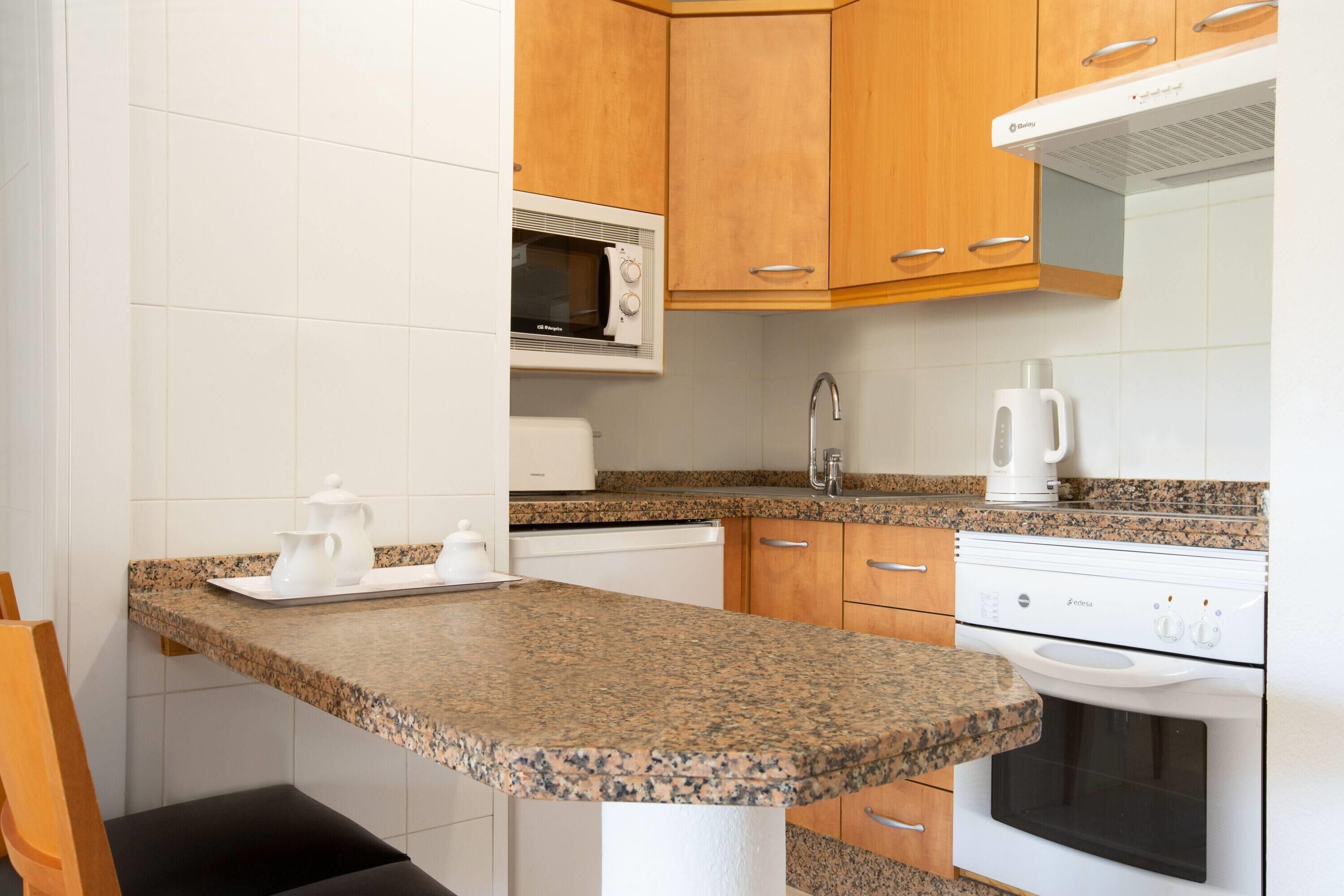 Una cocina compacta con encimeras de granito, microondas, cafetera y estufa.
