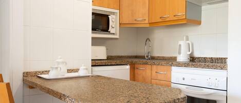 Una cocina compacta con encimeras de granito, microondas, cafetera y estufa.
