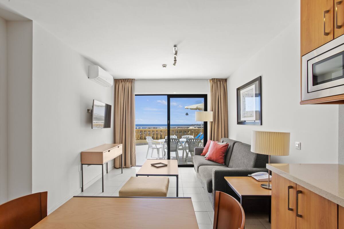Ein modernes Hotelzimmer mit Balkon, einer Couch, einem Esstisch und einer Küchenzeile.