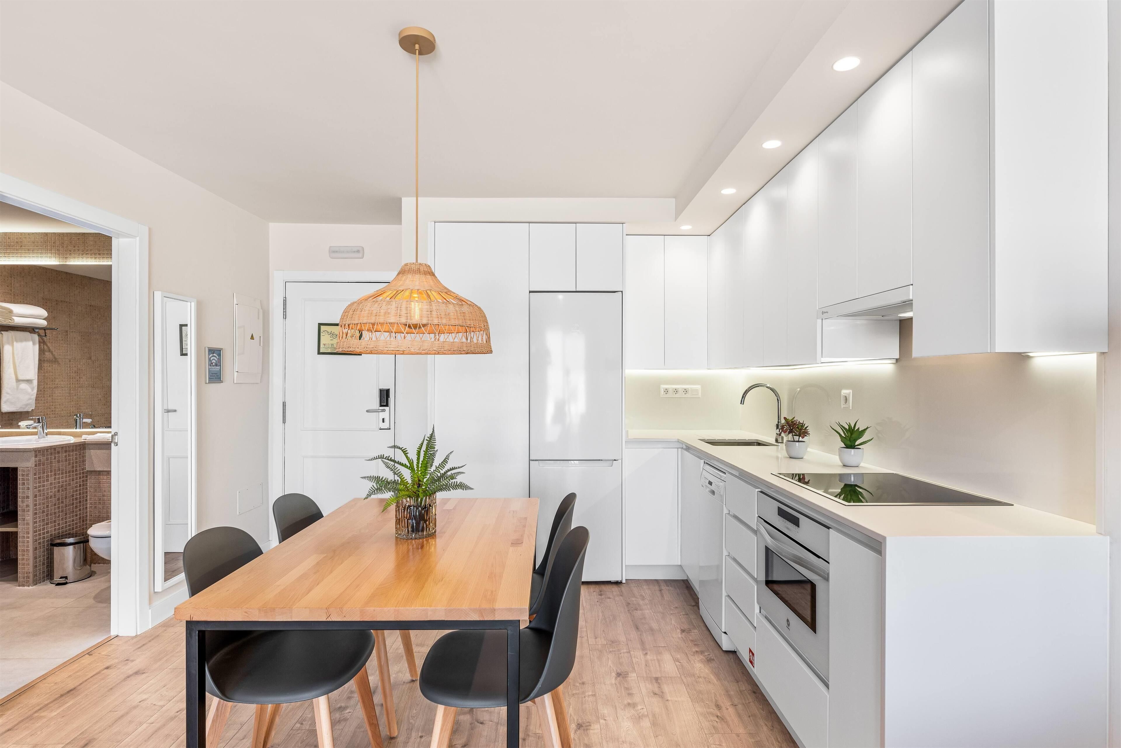Una cucina moderna con mobili bianchi, un tavolo da pranzo in legno, sedie nere e una lampada a sospensione.