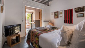 Een hotelkamer met een bed, een televisie op een houten standaard, en een deur naar een buitenruimte.