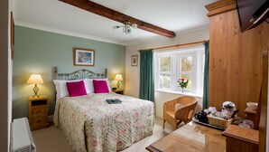 A bedroom with a bed, two bedside lamps, a wooden dresser, a wicker chair, and a window with curtains. - Well appointed cottage on a working hill farm (Otley)