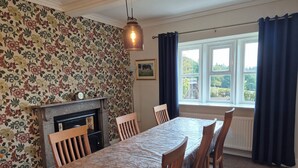 A dining room with a long table, chairs, a fireplace, and a window with curtains. - Well appointed cottage on a working hill farm (Otley)