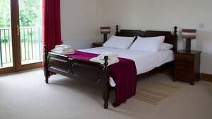 A bedroom with a bed, a nightstand, a lamp, a window with curtains, and a view of greenery outside.