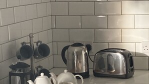A kitchen with white tiled backsplash, a wooden cutting board with teapot, cups, and a toaster.