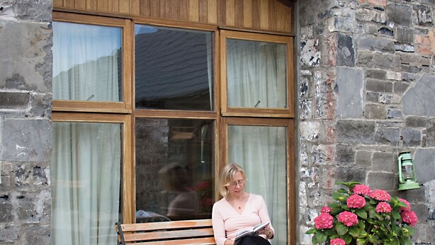 A woman sitting on a bench outside a building with large windows and a brick facade.
