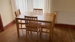 A dining area with a wooden table and chairs, a radiator, and a window with sheer curtains.
