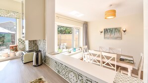 Una cocina luminosa con ventana, un área de comedor con sillas, una mesa y una pequeña isla con tostadora y hervidor.