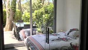 A bedroom with a bed, a glass door leading to an outdoor area with a table and chairs, and a tree. - T2 Golf Valescure, swimming pool, tennis & private garden (Saint-Raphaël)