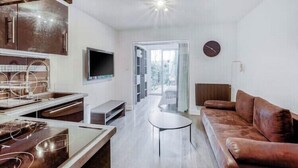 A modern living room with a brown leather sofa, a flat-screen TV mounted on the wall, and a kitchen area with stainless steel appliances. - T2 Golf Valescure, swimming pool, tennis & private garden (Saint-Raphaël)