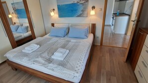 Een net opgemaakt bed met beddengoed met patroon en twee opgevouwen handdoeken, een houten hoofdbord en een klein nachtkastje.