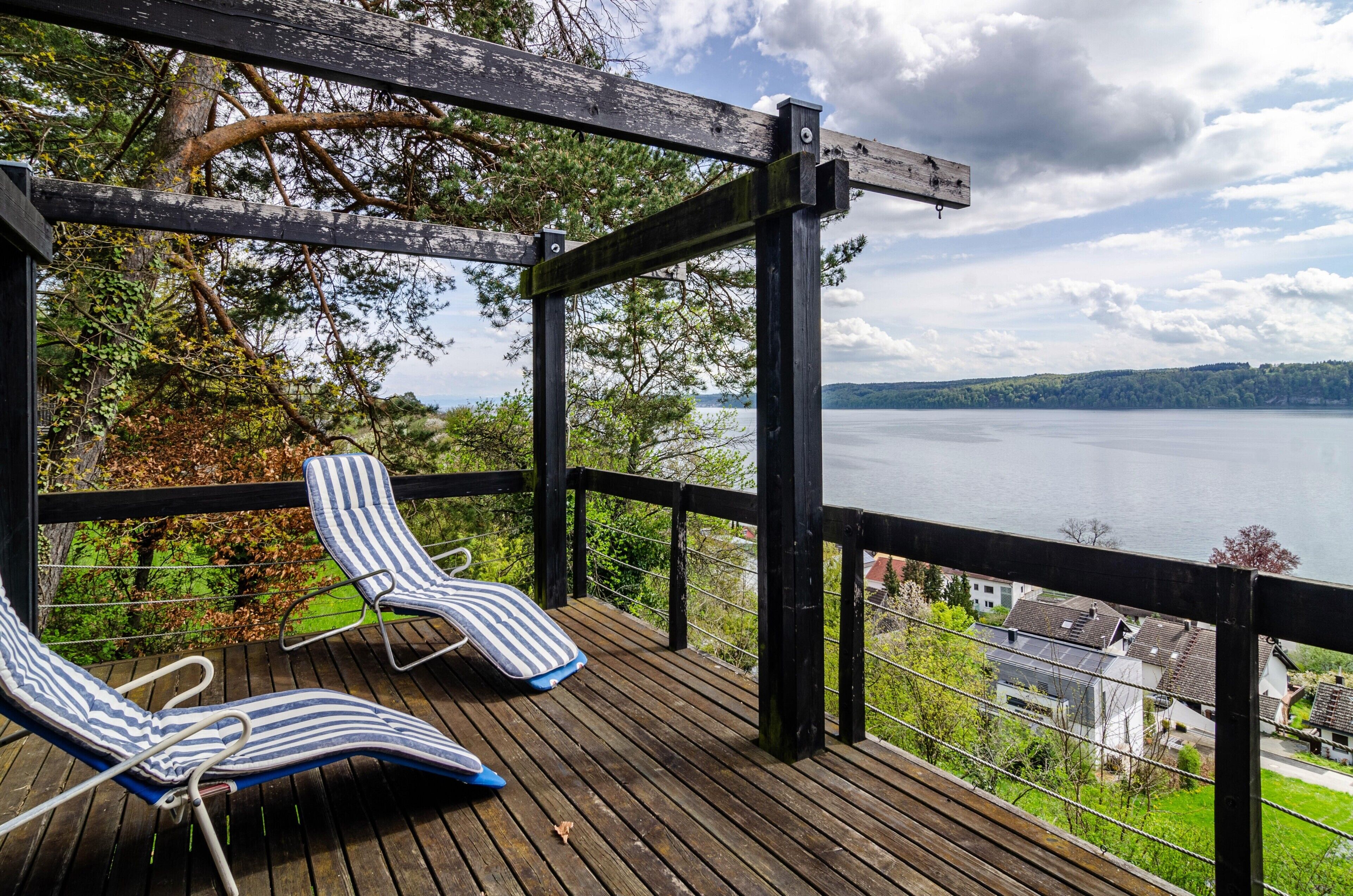 Terraza de madera con dos sillones reclinables a rayas con vista a un lago.