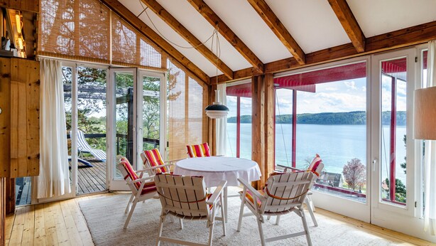 A wooden interior with a round table and chairs, large windows with a view of a lake, and a ceiling with exposed beams. - Holiday Home "Adlerhorst Über Dem Bodensee" with Panoramic Glazing, Terrace and Lake View (Sipplingen)