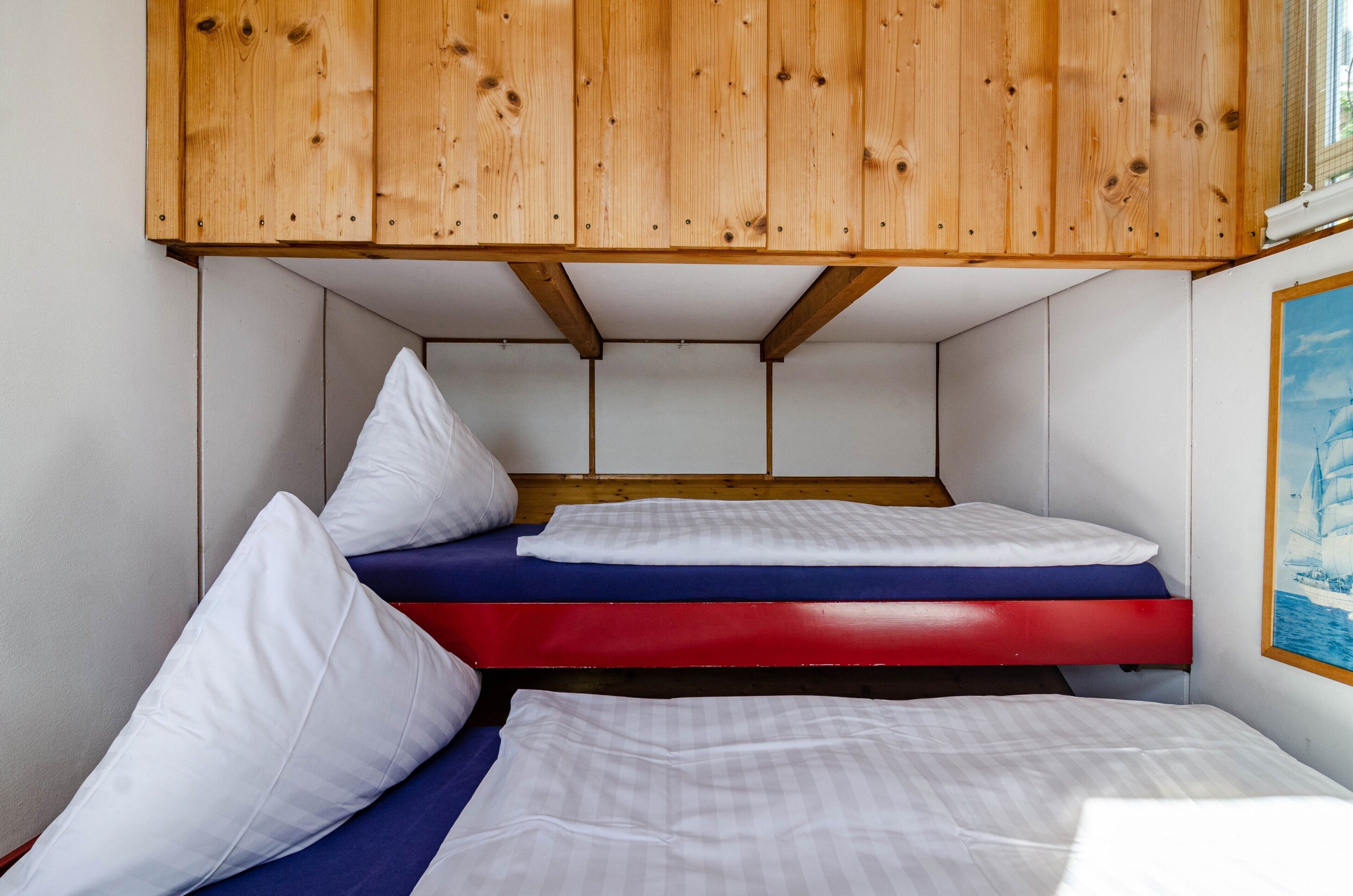 Un lit superposé avec une tête de lit en bois, des oreillers blancs et un matelas rouge.