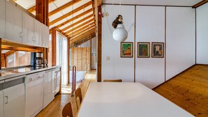 A kitchen with white cabinets, a wooden dining table, and a hanging light fixture. - Holiday Home "Adlerhorst Über Dem Bodensee" with Panoramic Glazing, Terrace and Lake View (Sipplingen)