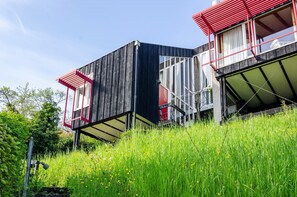A modern building with a sloped roof, large windows, and a red awning. - Holiday Home "Adlerhorst Über Dem Bodensee" with Panoramic Glazing, Terrace and Lake View (Sipplingen)