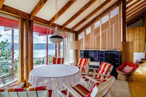A wooden interior with a round table and chairs, large windows, and a view of the outdoors.
