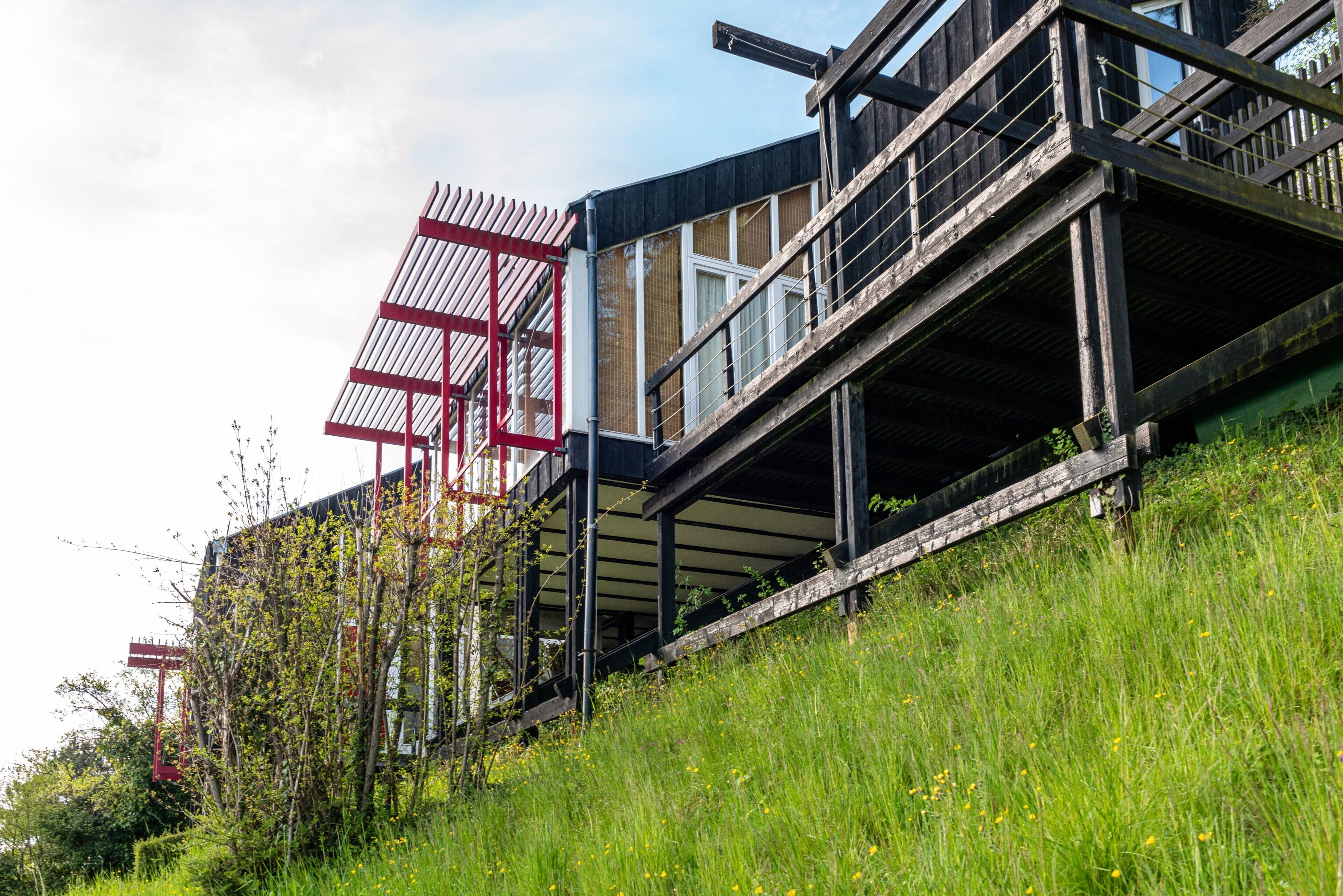 Een modern gebouw met een houten terras, glazen ramen en een rode constructie.