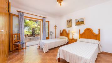 Un dormitorio con dos camas, una silla, una ventana con cortinas, un ventilador y una cruz en la pared.
